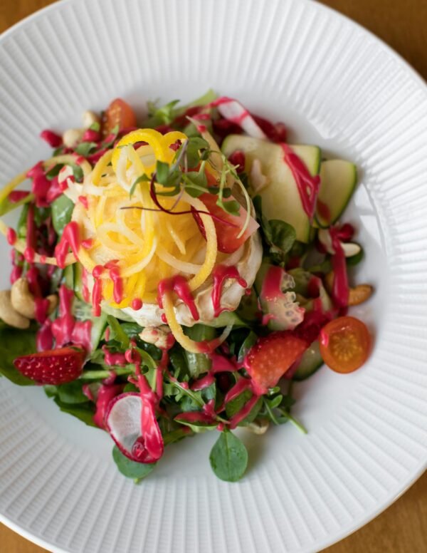 Colorful veggie salad with cashews, radish, and strawberries topped with a beet dressing.